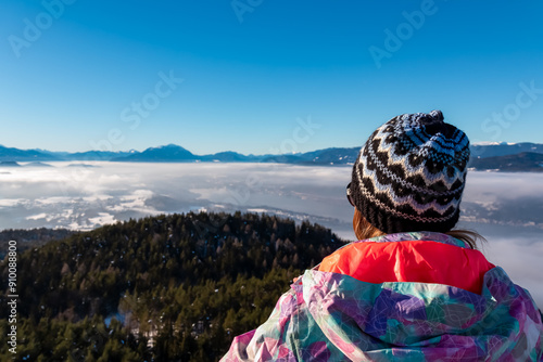 Tourist woman with panoramic view of fog covered lake Woerthersee in winter seen from observation tower Pyramidenkogel, Carinthia, Austria. Snow capped mountains Austrian Alps. Mystical atmosphere photo