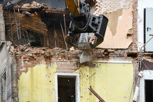 An excavator using a manipulator dismantles and destroys an old house. Construction site photo