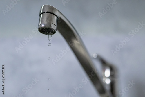 A drop of water drips from a leaky faucet. Close-up of a water dripping from a faucet