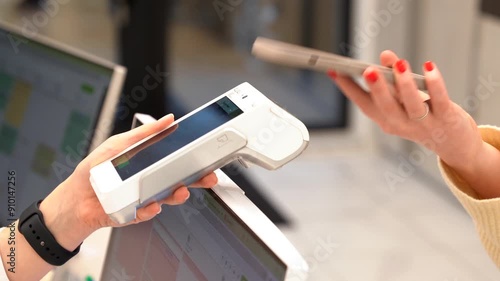 Pay by phone on electronic payment machine or card reader. E-money at cashless wallet. Female hand with pos-terminal and cellphone closeup. Client pays for the procedure in modern beauty clinic.