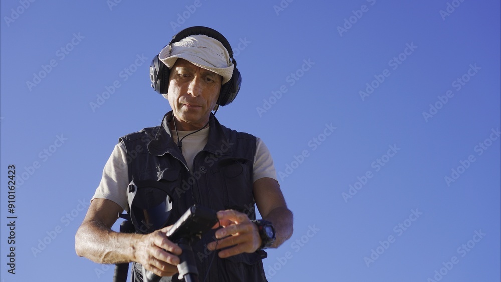 Waist-up view of the treasure hunter from below, preparing to search for buried items by setting up the metal detector on the beach.
