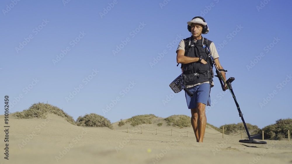 Young adult treasure hunter advancing towards target while searching for jewellery, with the Maspalomas sand dunes in the background. Young adult treasure hunter advancing towards target while searching for jewellery, with the Maspalomas sand dunes in the background.