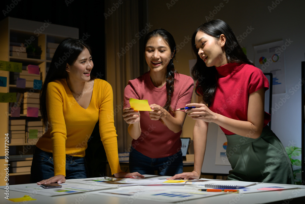 Fototapeta premium Young Women Collaborating on Creative Project in Modern Office Setting at Night