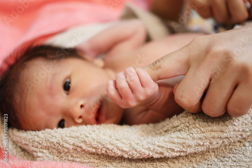A newborn baby lies holding its mother's finger.