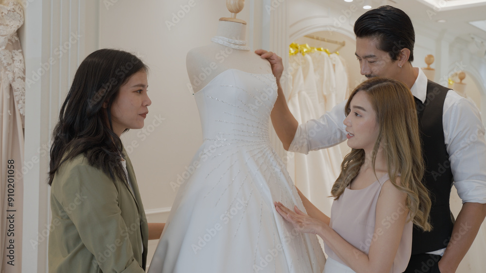 A woman is presenting a wedding dress for couples to choose from at wedding dress shop. A woman is presenting a wedding dress for couples to choose from at wedding dress shop.