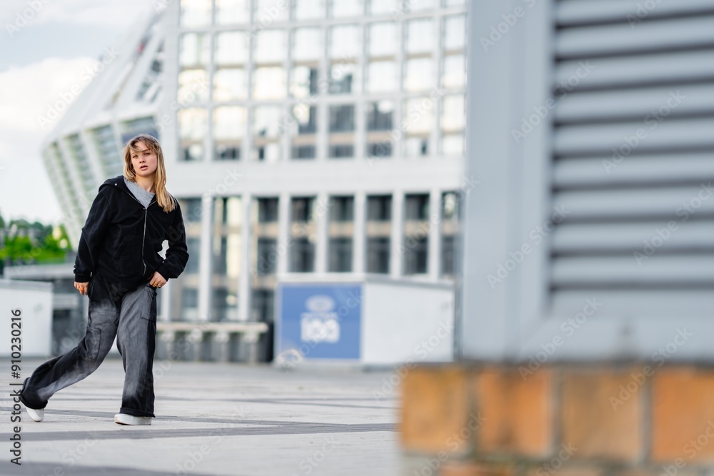 Young Girl Wearing Black Jacket and Gray Pants Walking in Modern Urban Environment