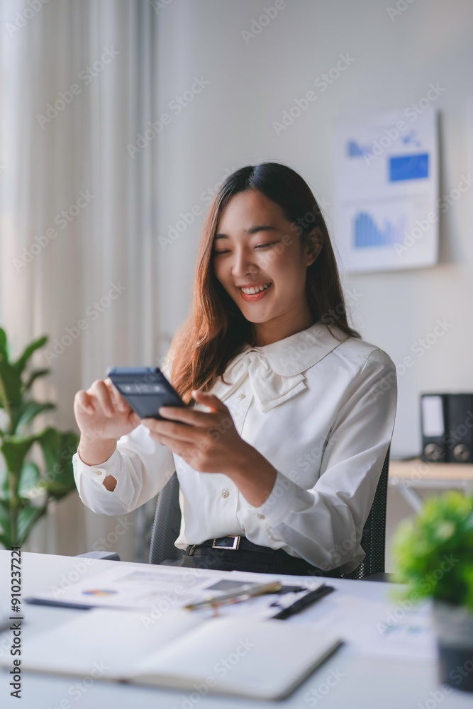 Young businesswoman is sitting at her desk and smiling while using her smartphone Young businesswoman is sitting at her desk and smiling while using her smartphone