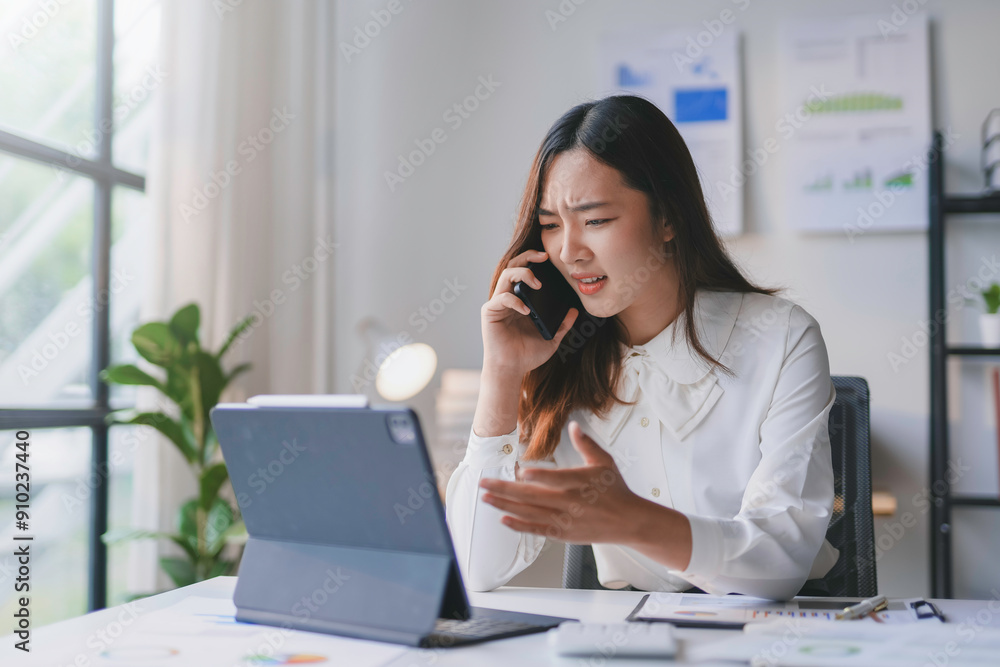 Businesswoman is having a stressful working day at the office while talking on the phone and looking at her tablet Businesswoman is having a stressful working day at the office while talking on the phone and looking at her tablet