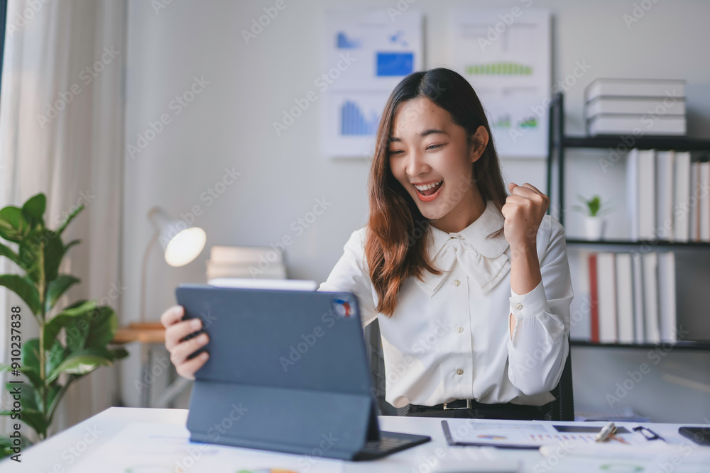 Happy businesswoman working with a tablet in a home office, raising her fist and smiling