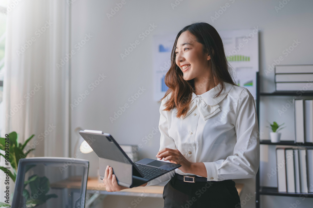 Young businesswoman is using her laptop and smiling while standing in her bright office Young businesswoman is using her laptop and smiling while standing in her bright office