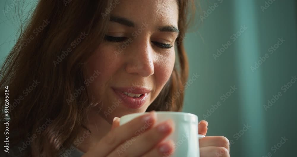 Close-up shot of a brunette girl blowing on a hot drink and then drinking tea from a white cup at home Close-up shot of a brunette girl blowing on a hot drink and then drinking tea from a white cup at home
