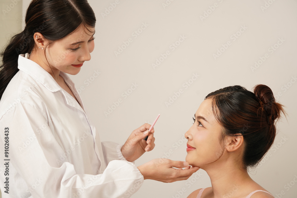 Asian female doctor in white dress, cosmetic surgeon touches the face of an Asian female patient who has a nose job and is assessing before cosmetic surgery and skin care in a cosmetic clinic. Asian female doctor in white dress, cosmetic surgeon touches the face of an Asian female patient who has a nose job and is assessing before cosmetic surgery and skin care in a cosmetic clinic.
