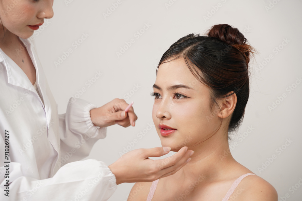 Asian female doctor in white dress, cosmetic surgeon touches the face of an Asian female patient who has a nose job and is assessing before cosmetic surgery and skin care in a cosmetic clinic.