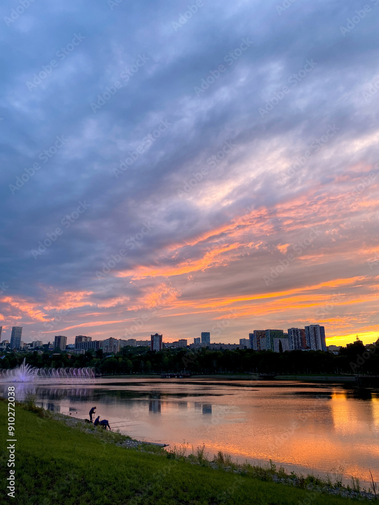 Fototapeta premium A stunning sunset gracefully casts its colors over a serene lake, while a vibrant city skyline stands majestically in the background, creating a picturesque blend of nature and urban life