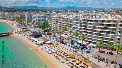 Aerial view of Antibes beach with tourists enjoying vacation in French Riviera. Plage d'Antibes Juan-les-Pins sandy beach with turquoise water and modern buildings in France.