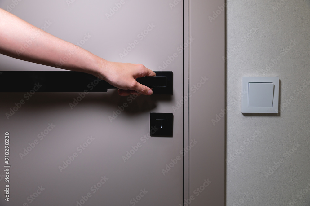 Close-up of a woman closing her hand on a modern gray door with a black handle and lock. White wall with a switch near the entrance. Privacy and security concept. Copy space Close-up of a woman closing her hand on a modern gray door with a black handle and lock. White wall with a switch near the entrance. Privacy and security concept. Copy space