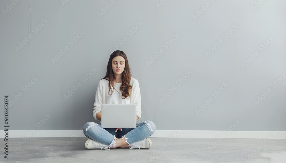 Young woman with modern laptop sitting on floor near grey wall Young woman with modern laptop sitting on floor near grey wall