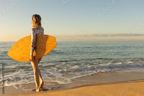 A woman is running in the ocean with a surfboard. The water is calm and the sky is clear photo