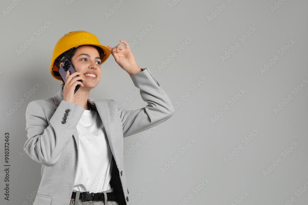 Engineer in hard hat talking on smartphone against grey background, space for text Engineer in hard hat talking on smartphone against grey background, space for text