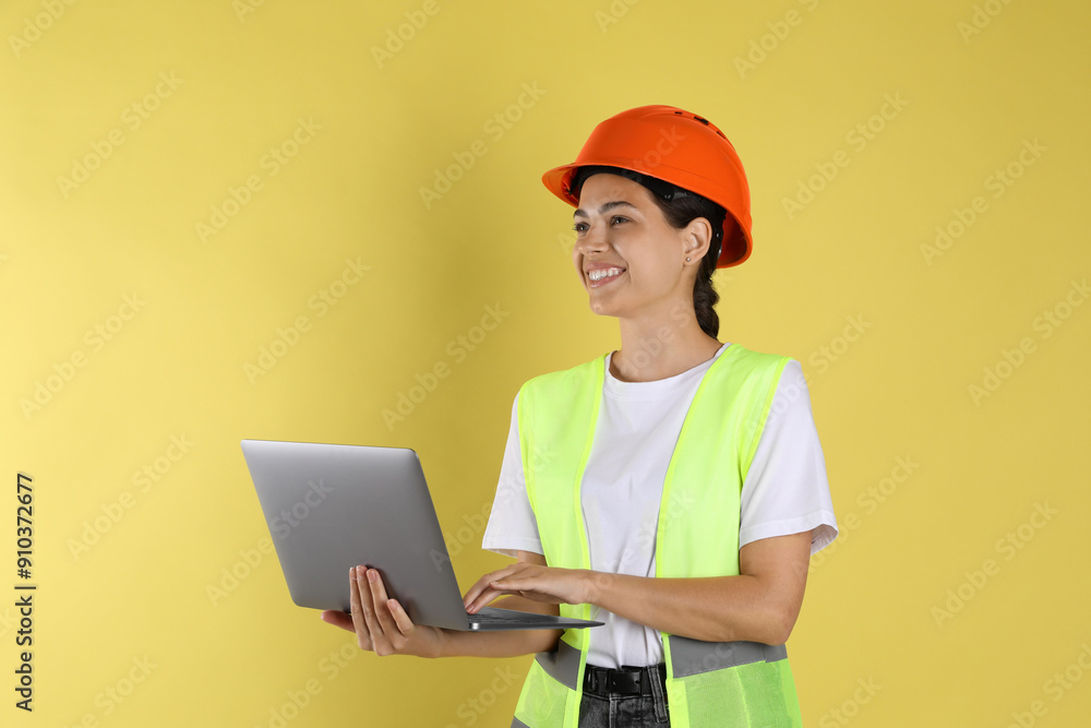 Engineer in hard hat with laptop on yellow background Engineer in hard hat with laptop on yellow background