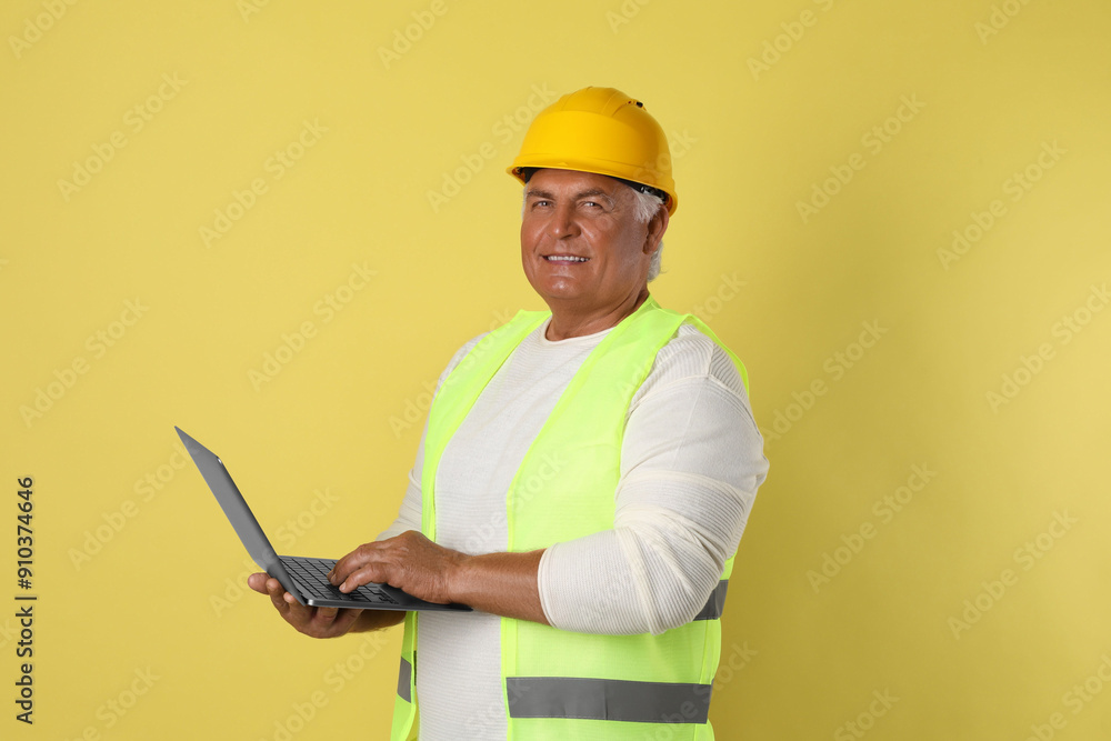 Engineer in hard hat with laptop on yellow background Engineer in hard hat with laptop on yellow background