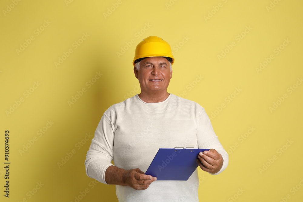 Engineer in hard hat with clipboard on yellow background Engineer in hard hat with clipboard on yellow background
