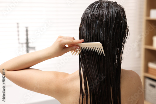 Woman combing her hair with applied mask in bathroom, back view