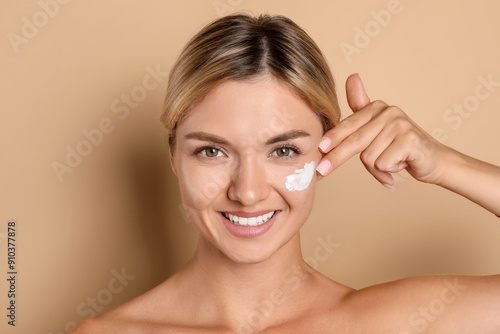 Beautiful woman applying cream on her face against beige background photo