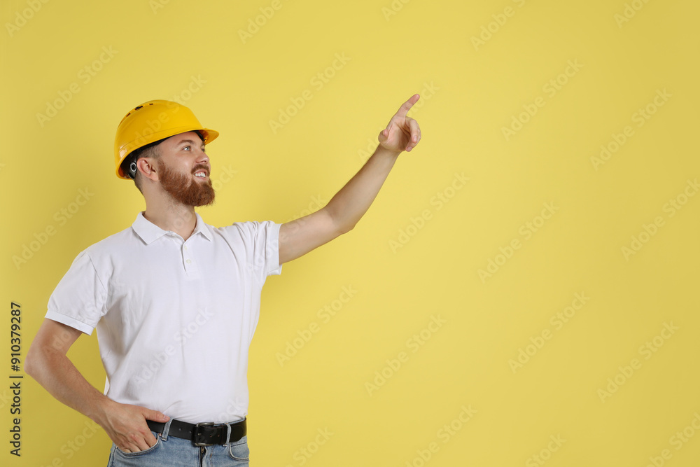 Engineer in hard hat pointing at something on yellow background, space for text Engineer in hard hat pointing at something on yellow background, space for text