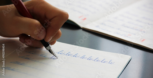 Detail of a child's left hand writing the syllables li and le with a fountain pen in a copybook. Concept for writing with the left hand. Back to school concept. Retro school writing in cursive.