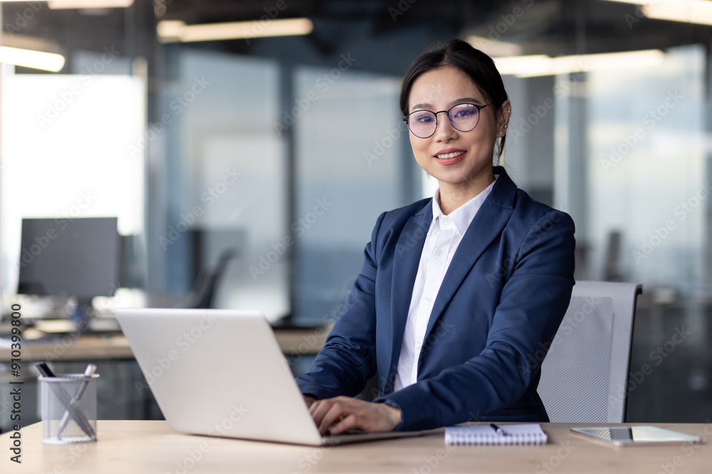 Professional Asian businesswoman working on a laptop at her desk in a modern office. She appears focused and confident, dressed in business attire, with a notepad and pen nearby. Professional Asian businesswoman working on a laptop at her desk in a modern office. She appears focused and confident, dressed in business attire, with a notepad and pen nearby.