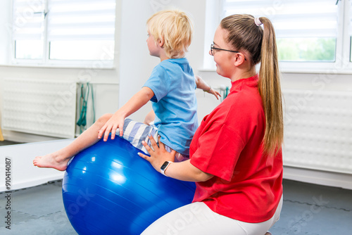 Young boy with female therapist exercising during physical therapy session. Child occupational physiotherapy. Bilateral coordination.