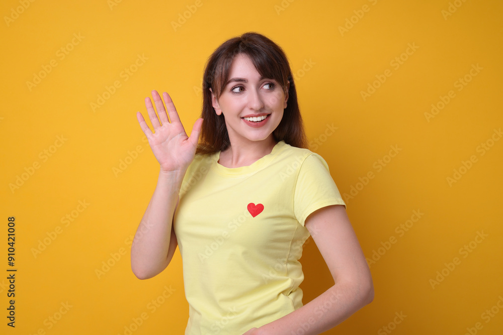 Happy young woman waving on orange background Happy young woman waving on orange background