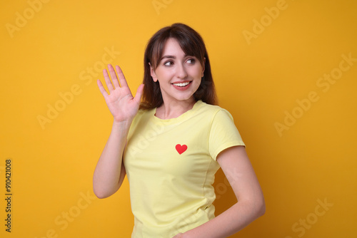 Happy young woman waving on orange background