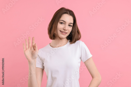 Happy teenage girl waving on pink background