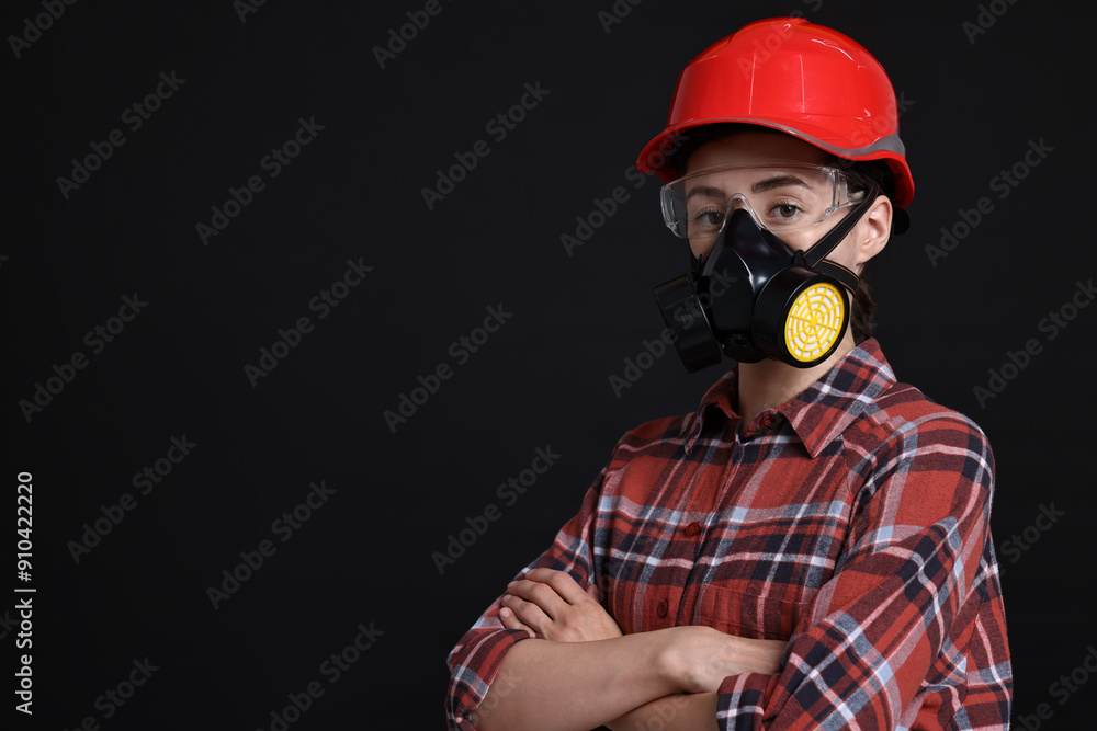 Woman in respirator, protective glasses and helmet on black background, space for text Woman in respirator, protective glasses and helmet on black background, space for text