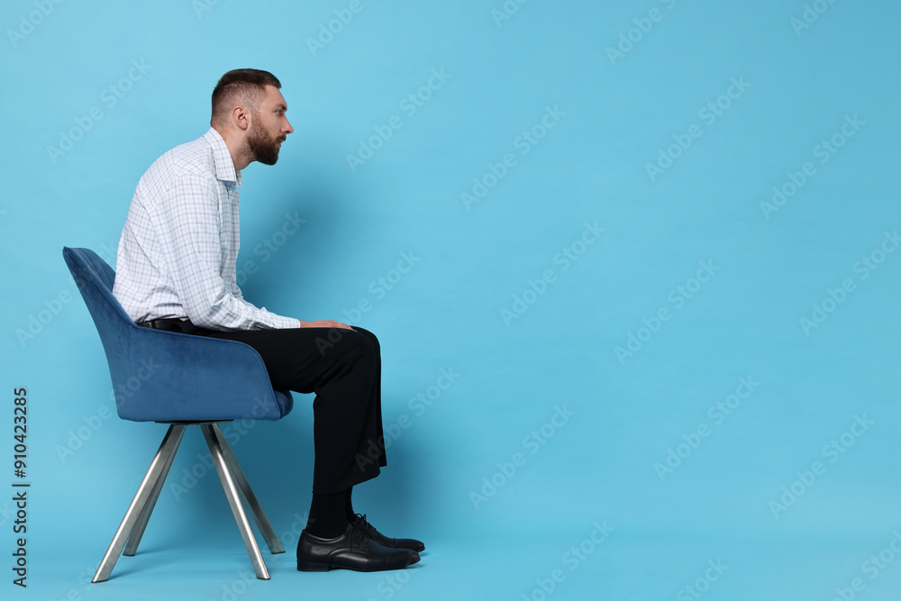 Man with poor posture sitting on chair against light blue background, space for text Man with poor posture sitting on chair against light blue background, space for text