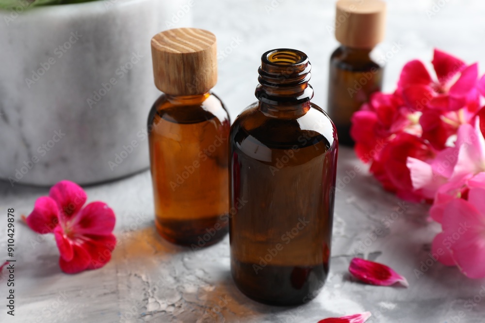 Bottles of geranium essential oil and beautiful flowers on light grey textured table, closeup Bottles of geranium essential oil and beautiful flowers on light grey textured table, closeup