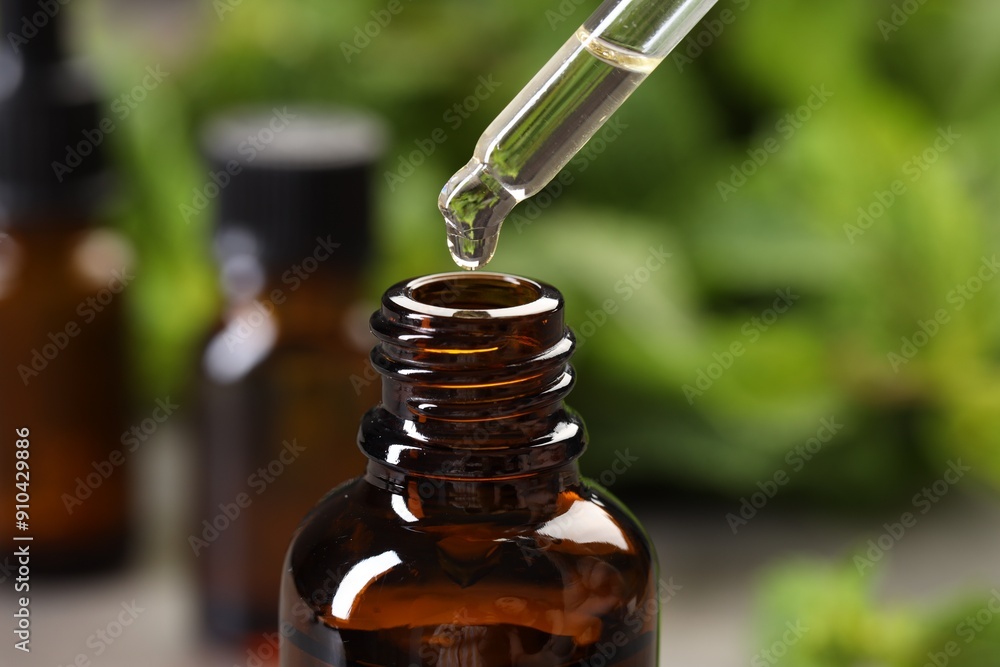 Dripping essential oil into bottle on blurred background, closeup Dripping essential oil into bottle on blurred background, closeup