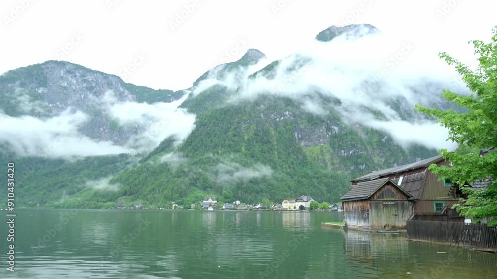 Misty clouds hover over the serene Hallstatt Lake, Austria, with wooden houses and lush green mountains creating a picturesque view. High quality 4k footage Misty clouds hover over the serene Hallstatt Lake, Austria, with wooden houses and lush green mountains creating a picturesque view. High quality 4k footage