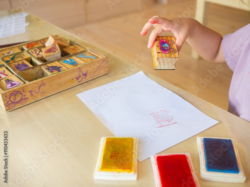 Children are playing with wooden stamps on white paper and colorful inks on table in a playroom to enhance skills, encourages and development.