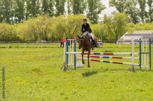 A young girl goes in for horse riding. A horse jumps over a barrier.