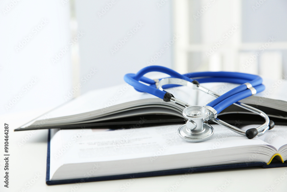 One medical stethoscope and books on white table, closeup