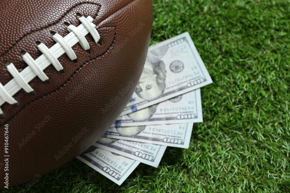 Obraz premium American football ball and dollar banknotes on green grass outdoors, closeup
