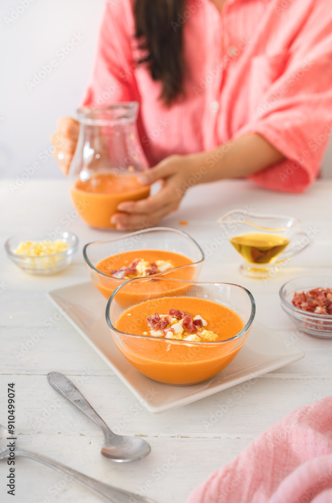 A woman serves freshly made salmorejo, topped with jamón and boiled egg, a staple of Spanish cuisine.