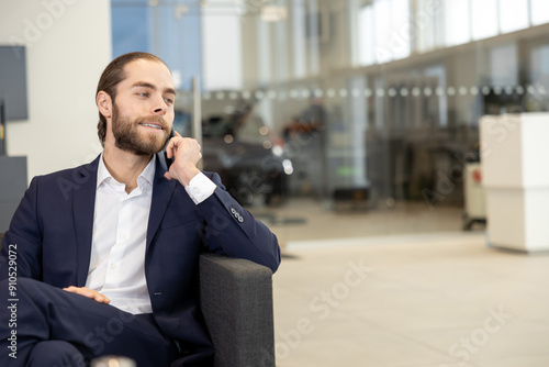 Salesman in suit talking on phone while sitting on sofa in modern dealership