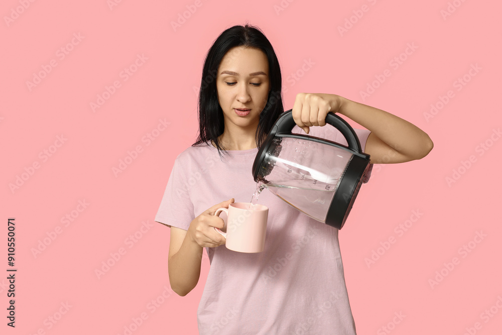 Beautiful young woman pouring hot water from modern electric kettle into cup on pink background Beautiful young woman pouring hot water from modern electric kettle into cup on pink background