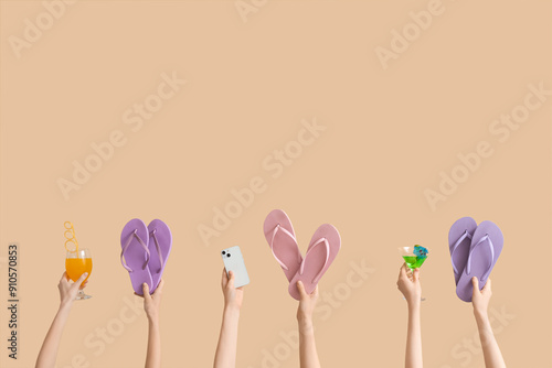 Hands holding three pairs of flip flops with cocktails and mobile phone on beige background