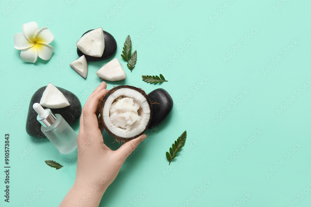 Female hand with coconut butter in fruit and bottle of cosmetic oil on turquoise background