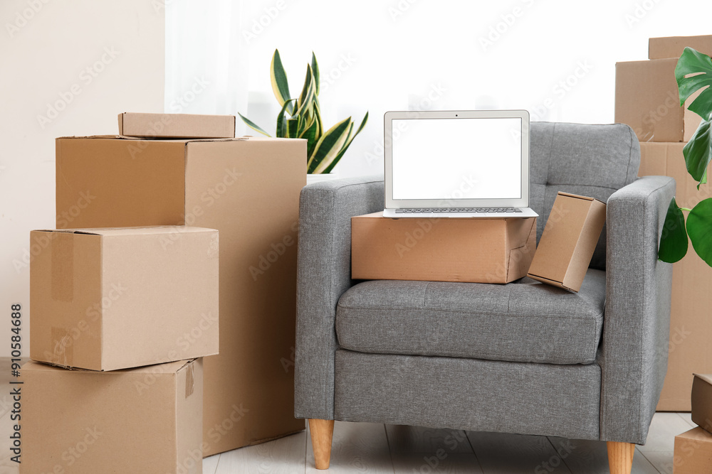 Blank laptop with moving boxes on armchair and plants near window in room Blank laptop with moving boxes on armchair and plants near window in room